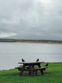 Empty bench by lake against sky