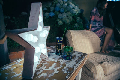 Drinks and star shaped light on table against woman sitting on sofa during party