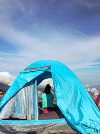 Rear view of women sitting in tent on mountain against cloudy sky