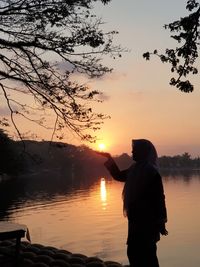 Silhouette man standing by lake against sky during sunset