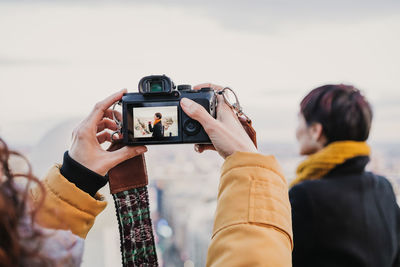 Woman photographing friend on camera against city