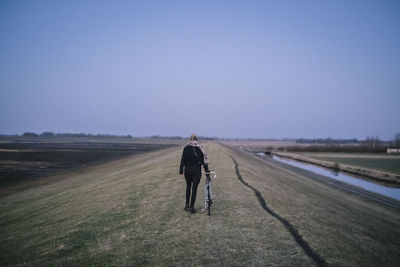 Rear view of woman walking on beach against clear sky