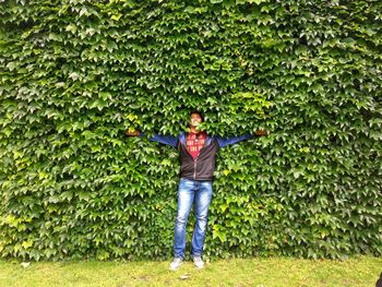 Man with arms outstretched standing against ivy
