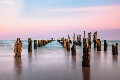 Wooden posts in sea against sky during sunset