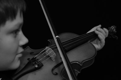 Man looking away while playing violin against black background