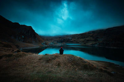 Rear view of man looking at lake against sky