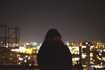 Rear view of woman by illuminated city against clear sky at night