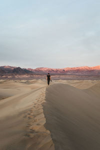 Man on sand dune in desert against sky