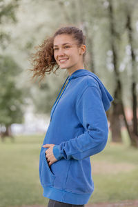 A european woman in a blue hoodie with a blue yoga mat chooses a place to do sports and meditation