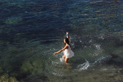 High angle view of playful woman standing in water at beach