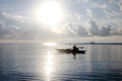 Man on boat in sea against cloudy sky