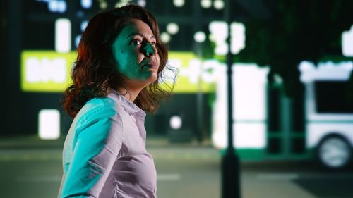 Side view of young woman looking away while standing in city