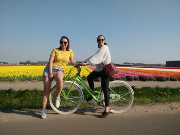 Full length of women standing with bicycle on street against clear sky