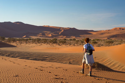 Rear view of woman walking on desert against sky