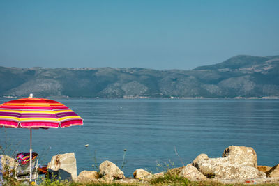 Deck chairs on rocks by sea against blue sky