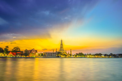 Scenic view of river by buildings against sky during sunset