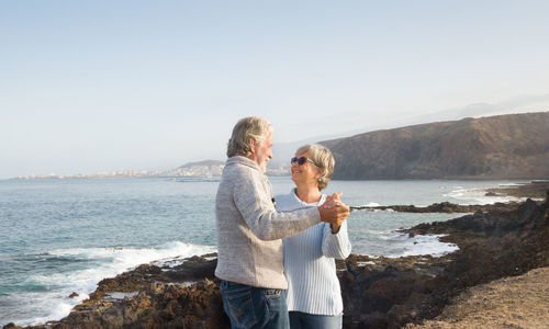 Happy senior couple dancing on rocky coastline