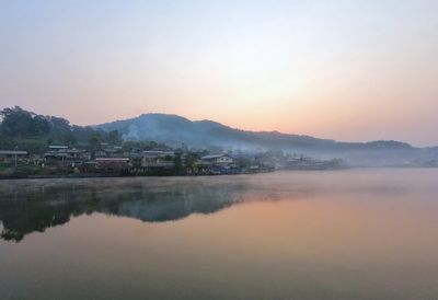 Scenic view of lake by buildings against sky during sunset