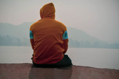 Rear view of man sitting by lake against sky