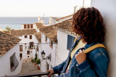 Rear view of woman standing by building against sky