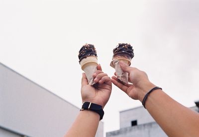 Cropped hand of couple holding ice cream against sky