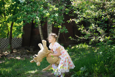 Cute european kid girl in dress with soft big toy dog in backyard, in park summer
