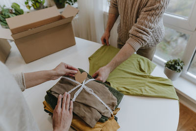 Fashion designer with colleague putting heart shaped card on folded clothes in workshop