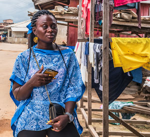 African woman from ghana in blue dress standing on the street in shama with mobile