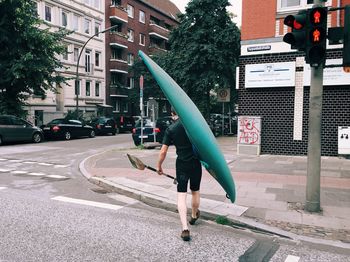 Rear view of man carrying canoe and oar on street in city