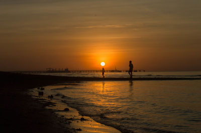 Silhouette people on beach against sky during sunset