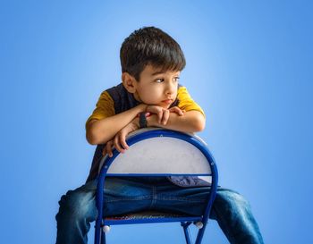 Portrait of boy looking away while standing against blue background