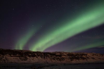 Scenic view of aurora polaris over snowcapped mountains against sky at night