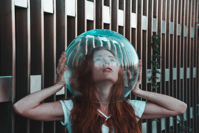 Close-up of young woman removing glass helmet from head against metallic railing