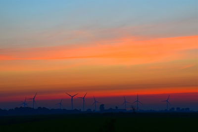 Silhouette wind turbines on field against orange sky