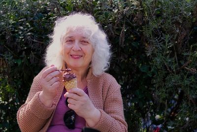 Elderly, curly, gray-haired lady eats ice cream from a waffle cone.