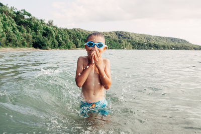 Portrait of shirtless boy in sea against sky