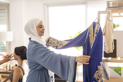 Happy fashion designer looking at blue wedding dress