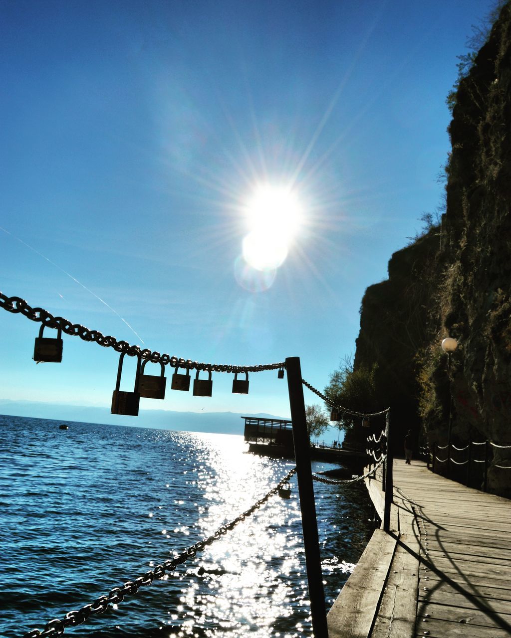 sun, water, sunlight, sunbeam, lens flare, sunny, sea, blue, built structure, sky, reflection, tranquility, railing, architecture, clear sky, tranquil scene, nature, pier, scenics, beauty in nature