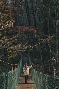 Woman standing on footbridge in forest