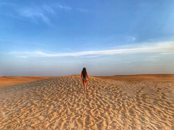 Rear view of seductive woman walking on sand in desert against sky