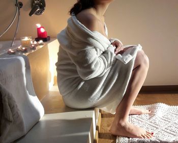 Low section of woman wearing bathrobe while sitting in bathroom