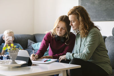 Mother helping daughter study while son using phone at home