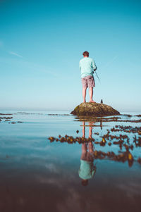 Rear view of man standing by sea against sky