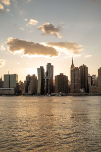 Buildings by river against sky during sunset