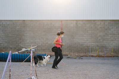 Obedient purebred border collie dog running during agility training with unrecognizable female instructor