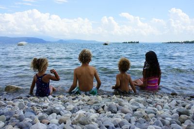 Rear view of siblings sitting on shore at beach