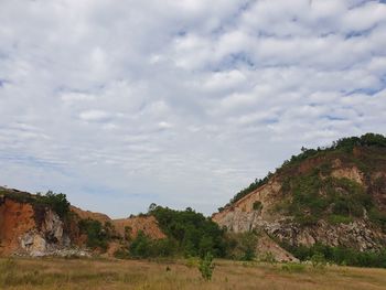 View of trees on landscape against cloudy sky