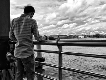 Rear view of man standing at railing against lake