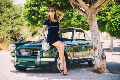 Full length portrait of woman wearing sunglasses while sitting on tree