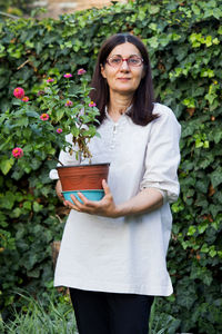Portrait of woman holding potted plant while standing against plants
